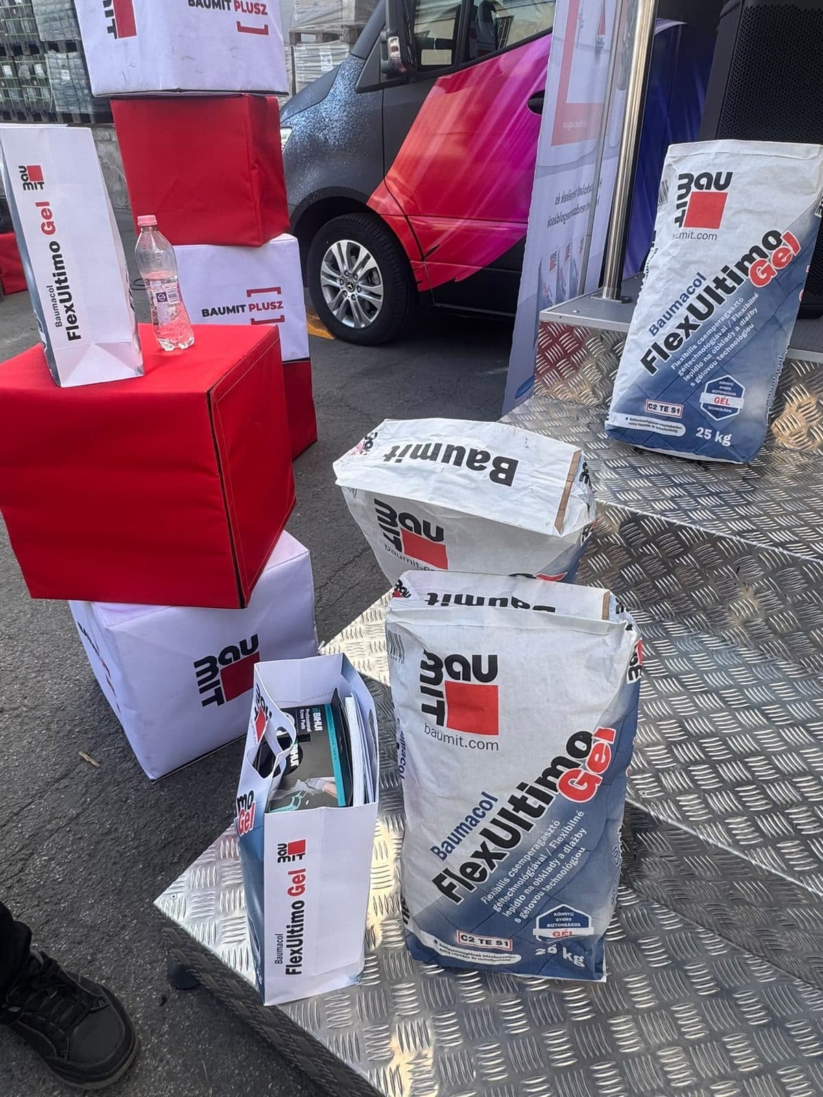 Baumit termékek zsákjai és vörös bemutató-kockák a Roadshow teherautója mellett